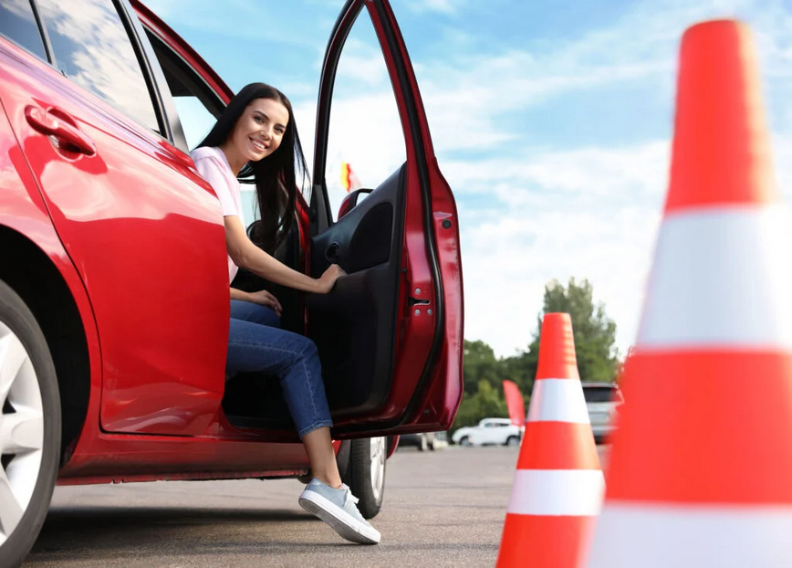 carousel slider image of a young female with her right leg out of a parked vehicle with door open smiling around tester centre cones.