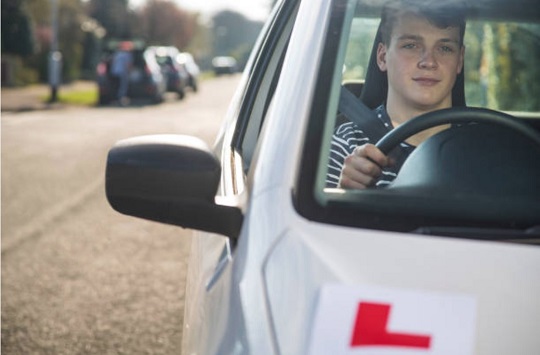 An image of a young male learner driver in a white coloured learner vehicle taken from the front.