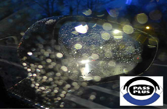 Image of a drivers wing mirror on a raining evening as seen from the drivers seat window.